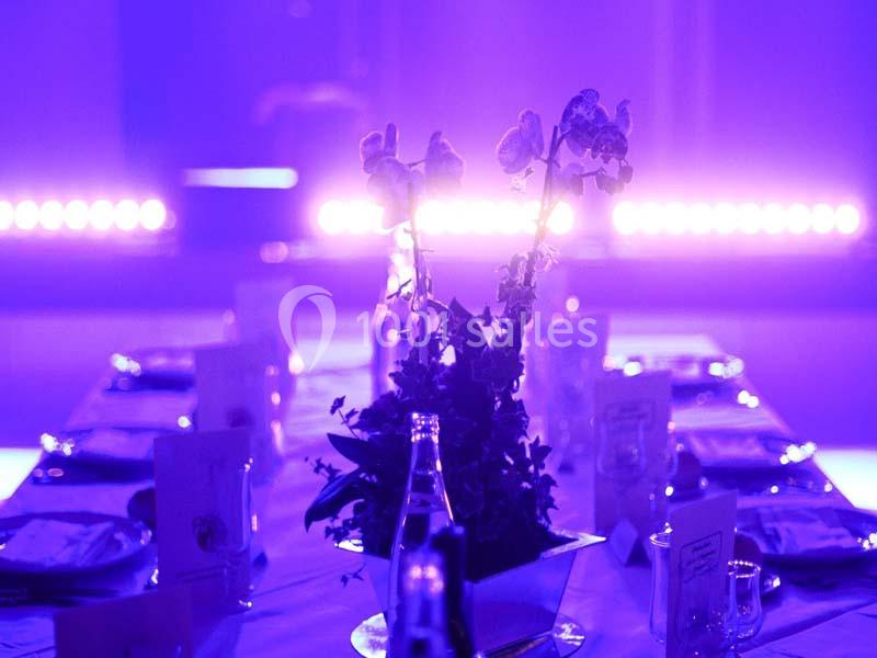 Centre de table floral sur une table dressée, éclairée par une lumière violette tamisée.