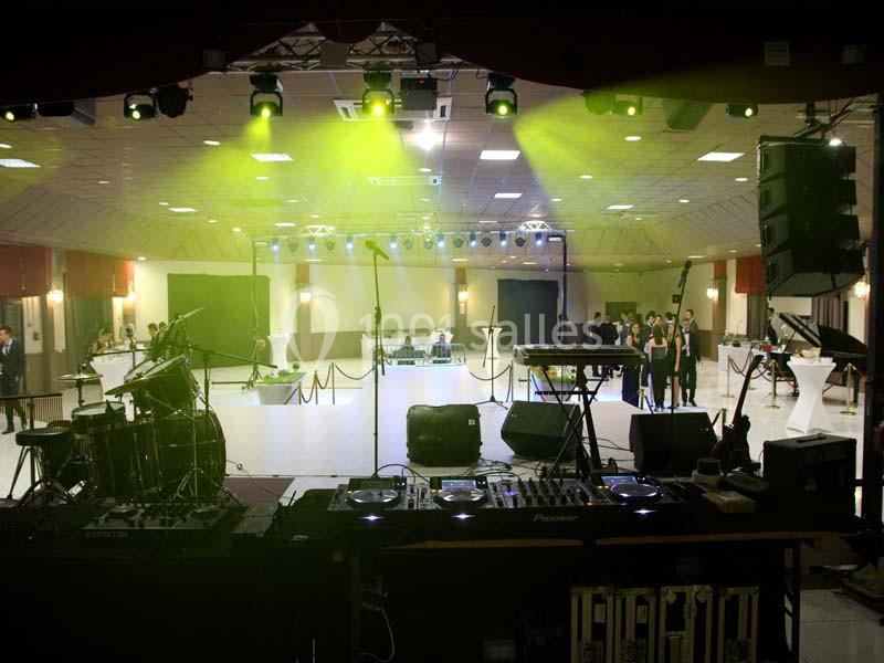 Salle de réception avec scène équipée d'instruments de musique, éclairages colorés et espace pour les invités.