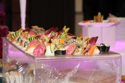 Plateau de sushis variés avec saumon, riz, légumes et feuilles d'endive, présenté sur un support transparent.