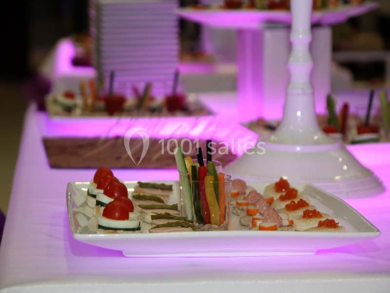 Plateau de bouchées apéritives variées avec légumes, fromage, saumon et tomates, présenté sur une table éclairée en violet.
