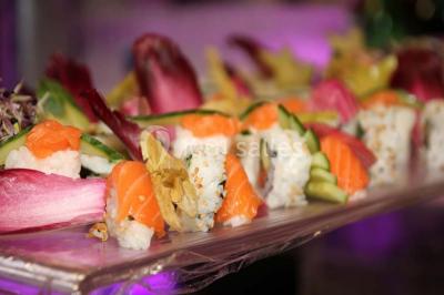 Plateau de sushis variés avec saumon, riz, légumes et feuilles d'endive, présenté sur un support transparent.
