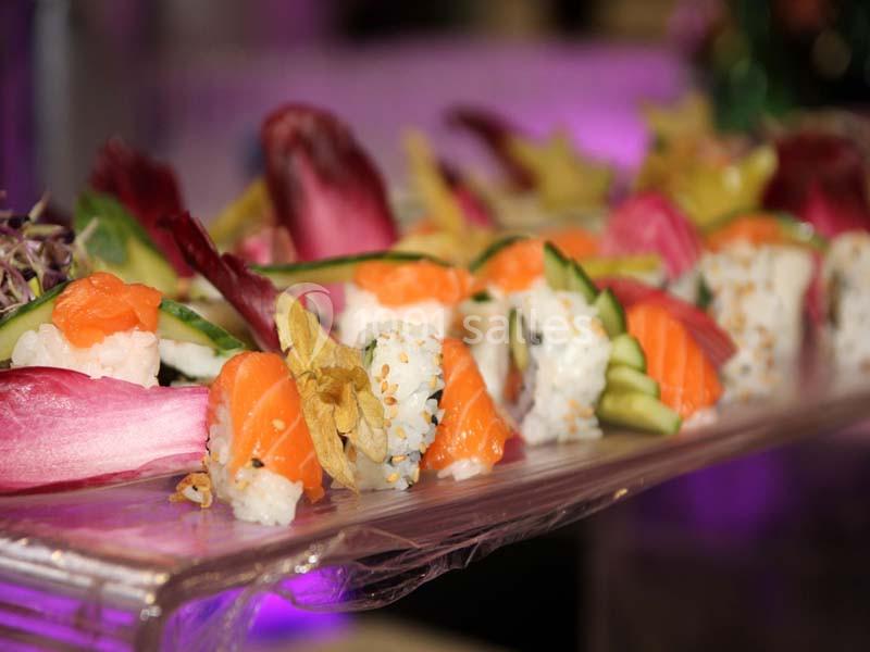 Plateau de sushis variés avec saumon, riz, légumes et feuilles d'endive, présenté sur un support transparent.