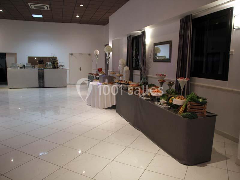 Buffet varié disposé dans une salle lumineuse avec sol carrelé blanc et tables décorées.