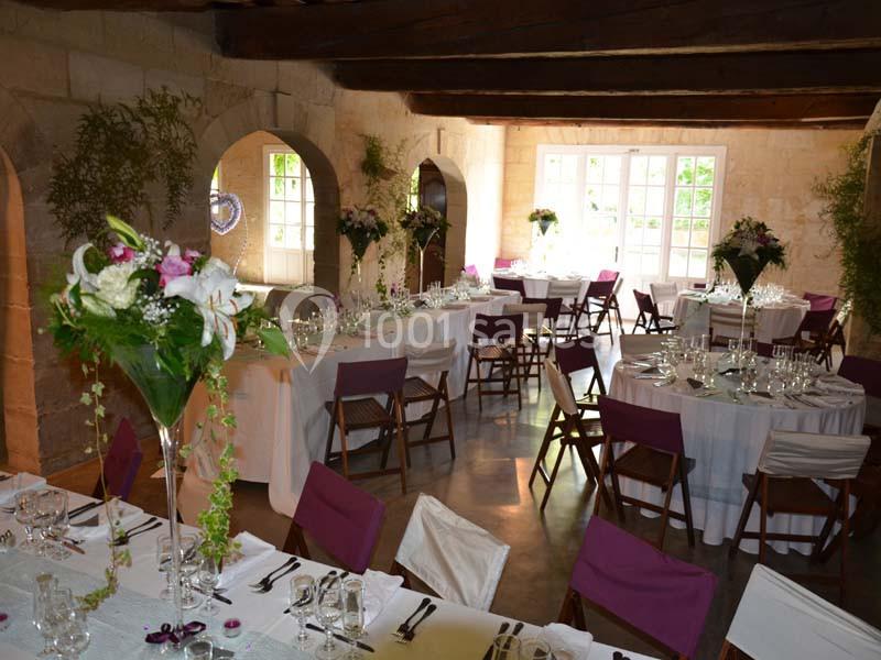 Salle de réception décorée avec des tables rondes et rectangulaires, nappes blanches, chaises violettes et arrangements…