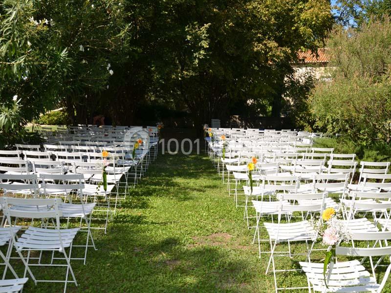 Chaises blanches alignées en extérieur, formant une allée centrale, entourées de verdure sous un ciel dégagé.