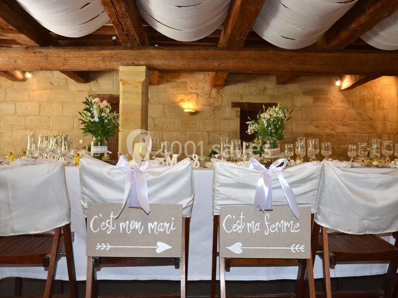 Chaises décorées pour un mariage, avec des panneaux indiquant ’C'est mon mari’ et ’C'est ma femme’, dans une salle rustique.