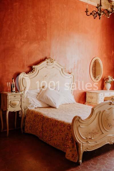 Chambre avec lit ancien en bois sculpté, murs rouges, tables de chevet assorties et miroir ovale.