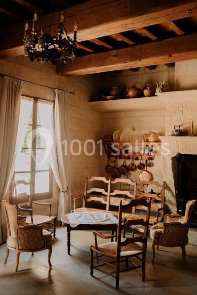 Salle à manger rustique avec table ronde, chaises en bois, cheminée en pierre et étagères garnies d'ustensiles en cuivre.