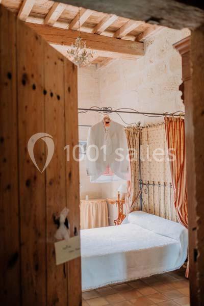 Chemise blanche suspendue sur un cintre dans une chambre lumineuse avec lit, rideaux et plafond en poutres apparentes.