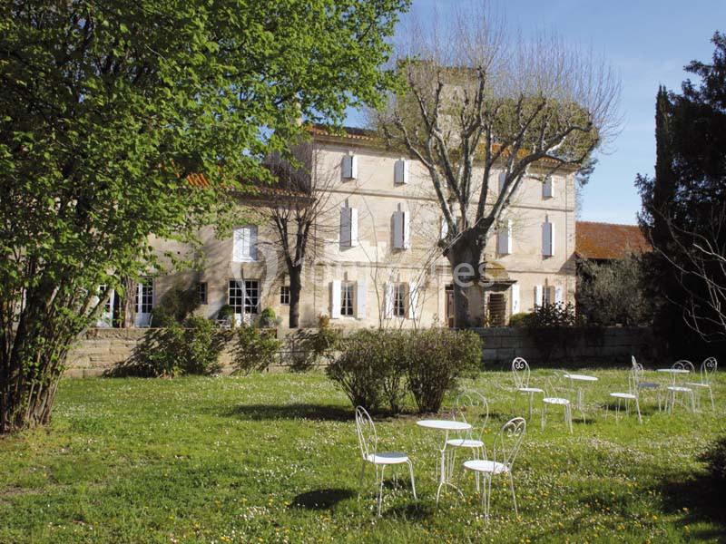 Façade d'une maison en pierre entourée d'un jardin verdoyant avec des tables et chaises blanches disposées sur la pelouse.