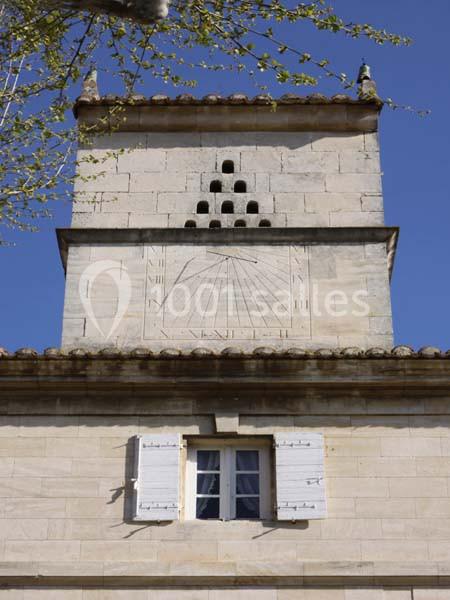 Façade en pierre avec un cadran solaire, des ouvertures pour pigeons et une fenêtre à volets blancs.