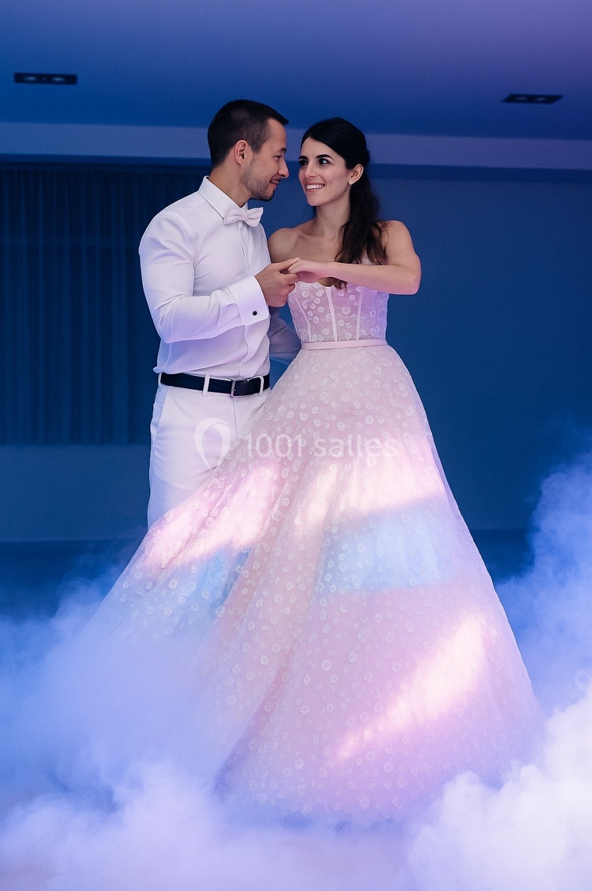 Un couple élégant danse dans une ambiance romantique avec éclairage coloré et fumée au sol.
