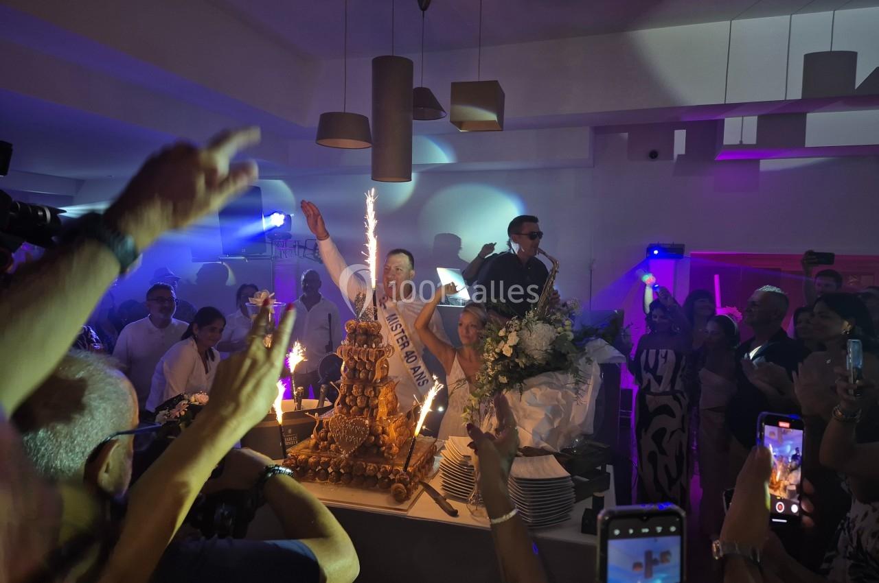 Un homme célèbre un anniversaire avec un gâteau éclairé par des bougies étincelantes, entouré d'invités festifs.