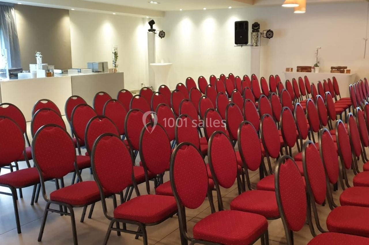 Salle aménagée avec des rangées de chaises rouges alignées, prête pour un événement ou une réunion.