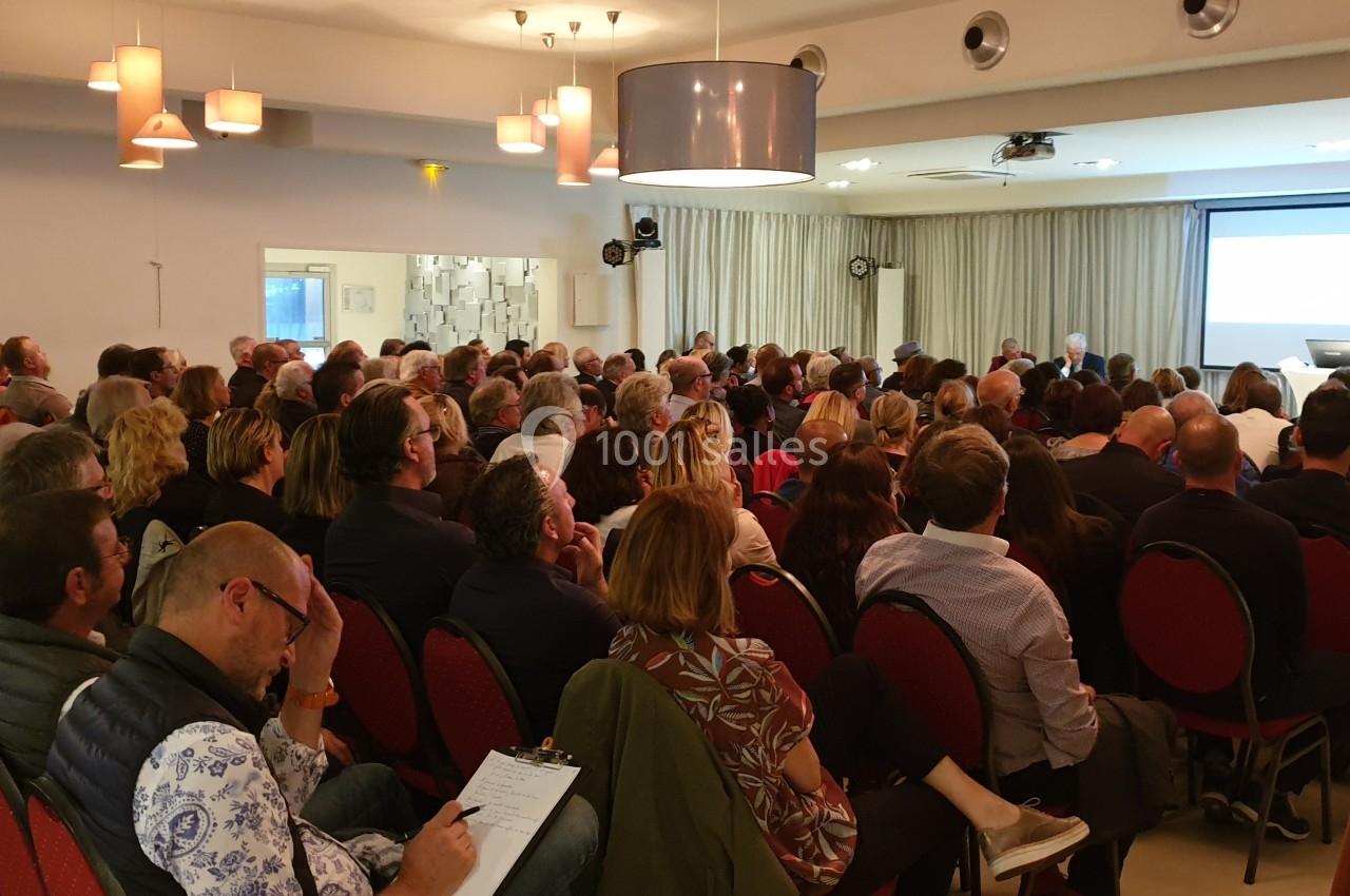 Un groupe de personnes assises dans une salle de conférence, écoutant un intervenant devant un écran de projection.