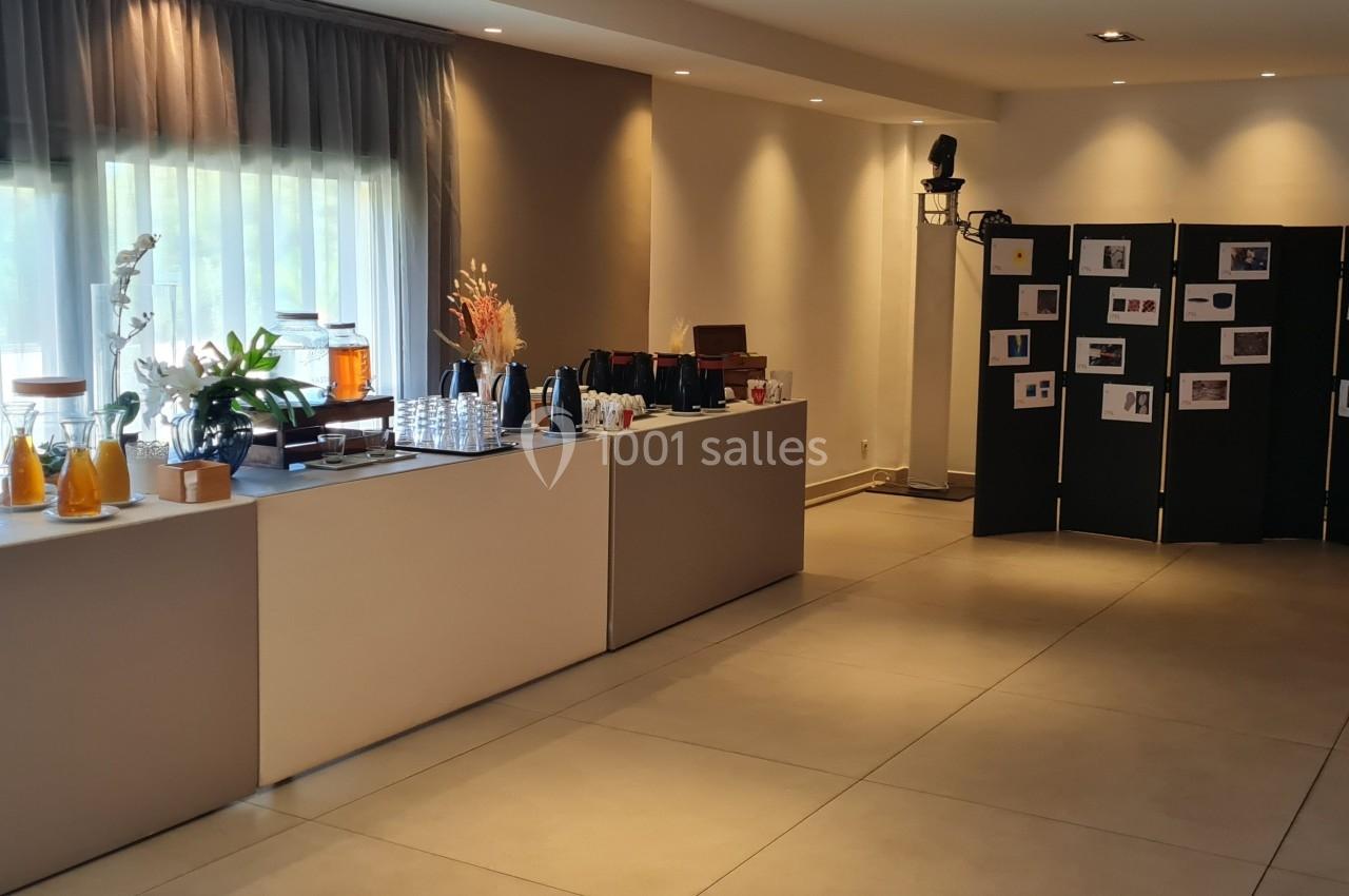 Buffet avec boissons, verrerie et décorations, installé dans une salle lumineuse avec un paravent affichant des photos.