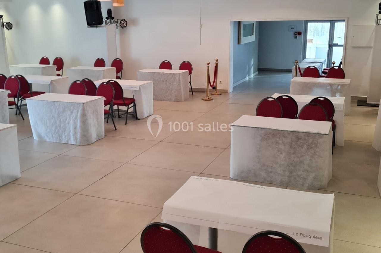 Salle de conférence lumineuse avec des tables recouvertes de nappes blanches et des chaises rouges alignées.