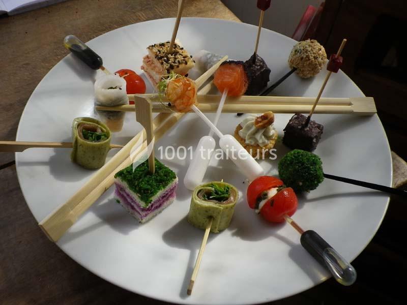 Assortiment de bouchées apéritives variées présentées sur un plateau rond avec des brochettes et pipettes.