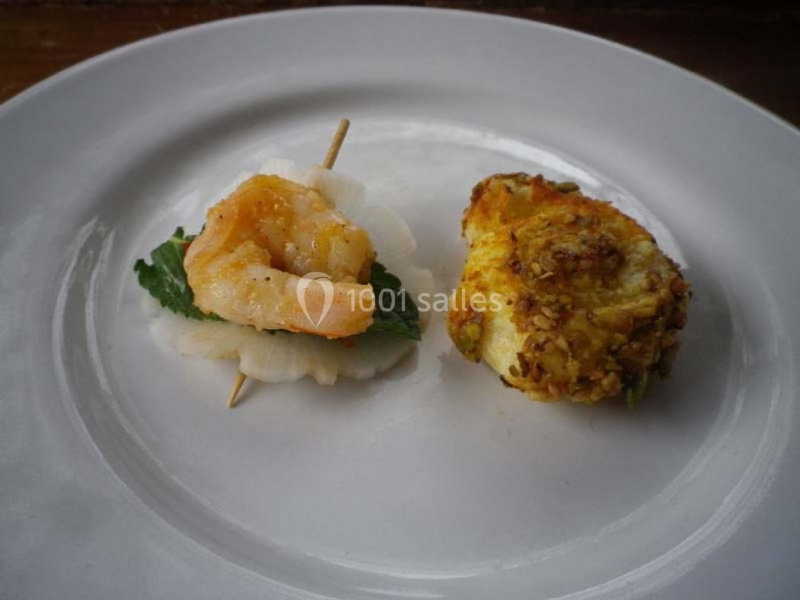 Une crevette sur une feuille verte et une tranche de radis à gauche, un petit gâteau salé doré à droite, sur une assiette…
