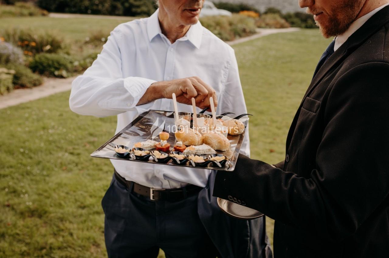 Un homme en costume tient un plateau de bouchées apéritives tandis qu'un autre homme en chemise en prend une.