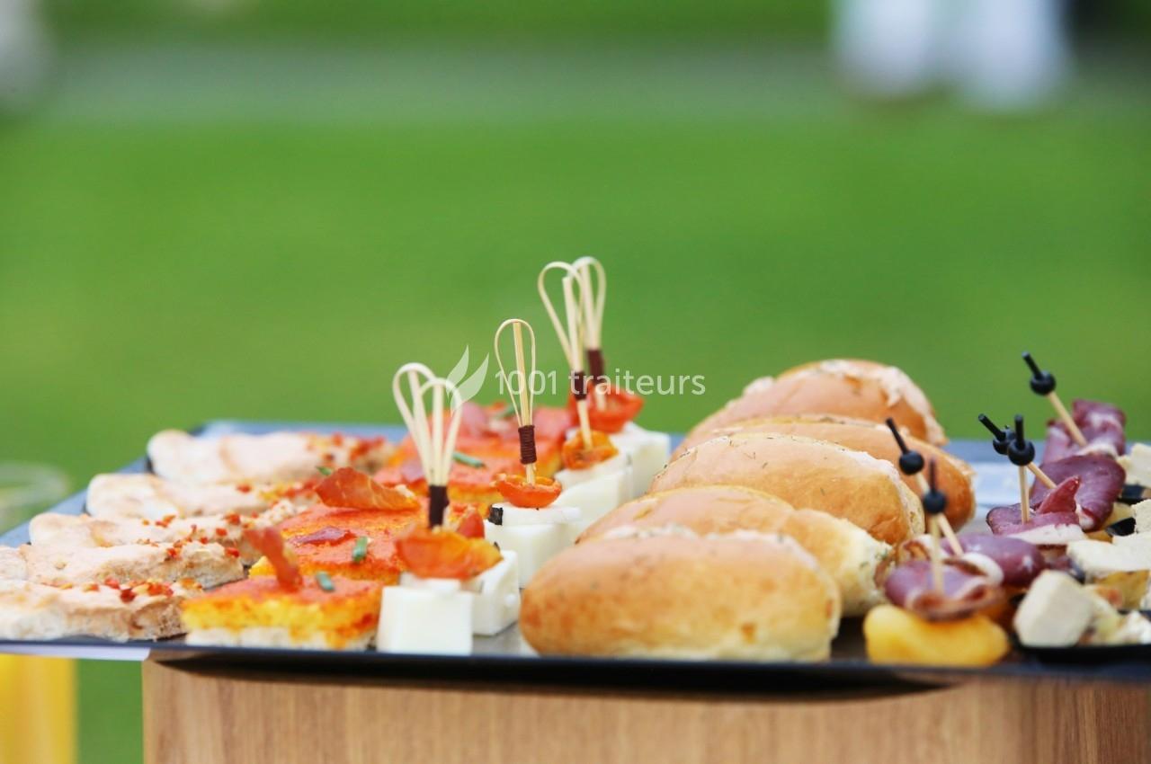 Plateau de bouchées apéritives variées comprenant mini-sandwichs, brochettes et tartines, présenté en extérieur.