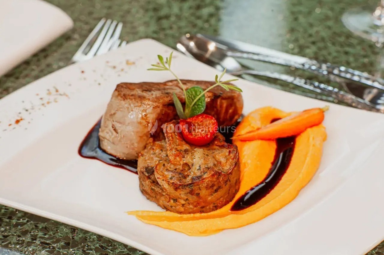 Assiette gastronomique avec filet de viande, purée de carottes, garniture de légumes et sauce décorative.