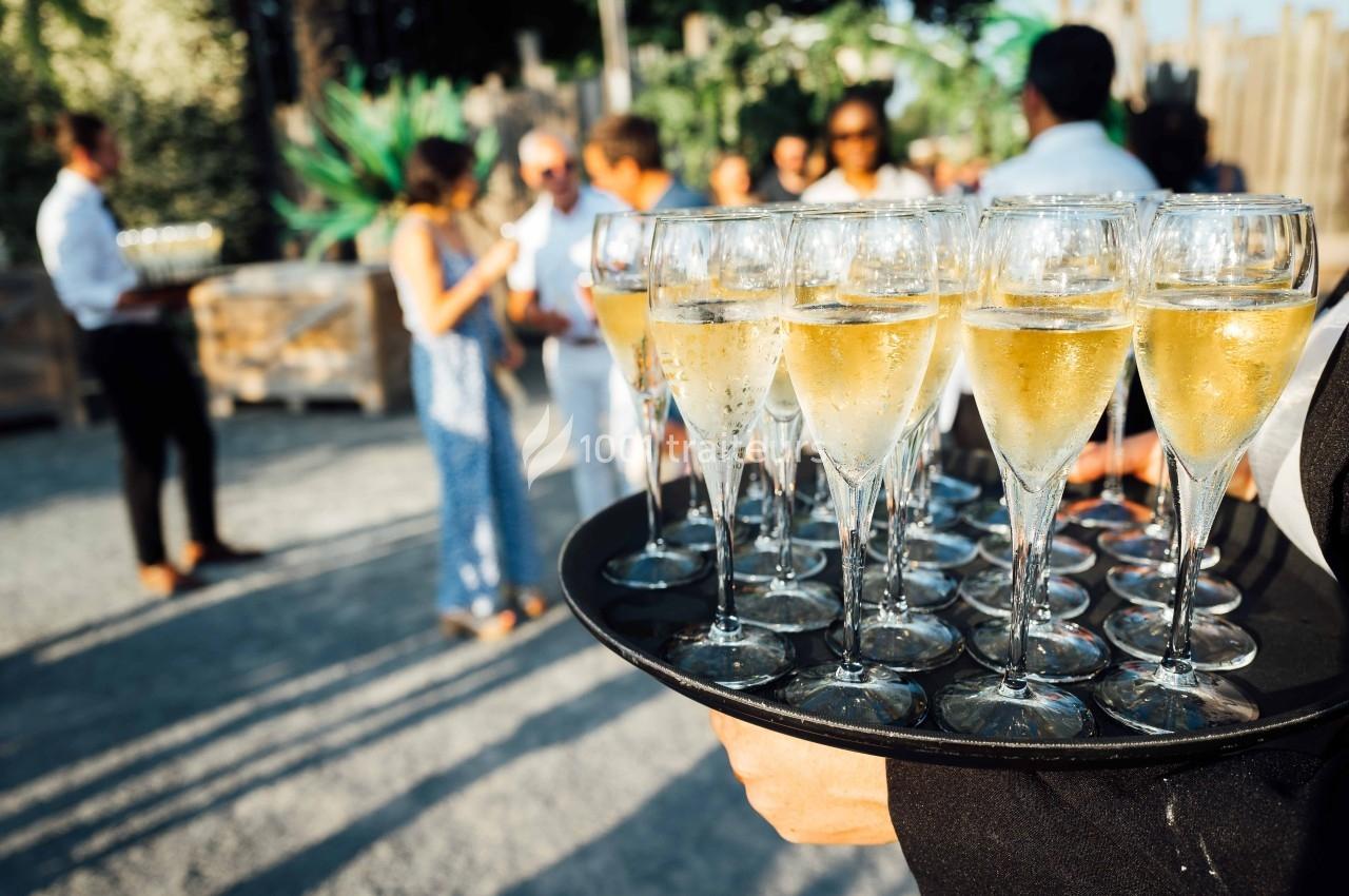 Plateau de flûtes de champagne tenu par un serveur lors d'un événement en extérieur avec des invités en arrière-plan.