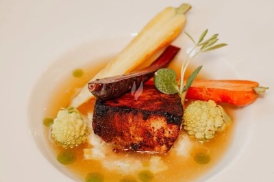 Assiette gastronomique avec filet de viande, purée de carottes, garniture de légumes et sauce décorative.