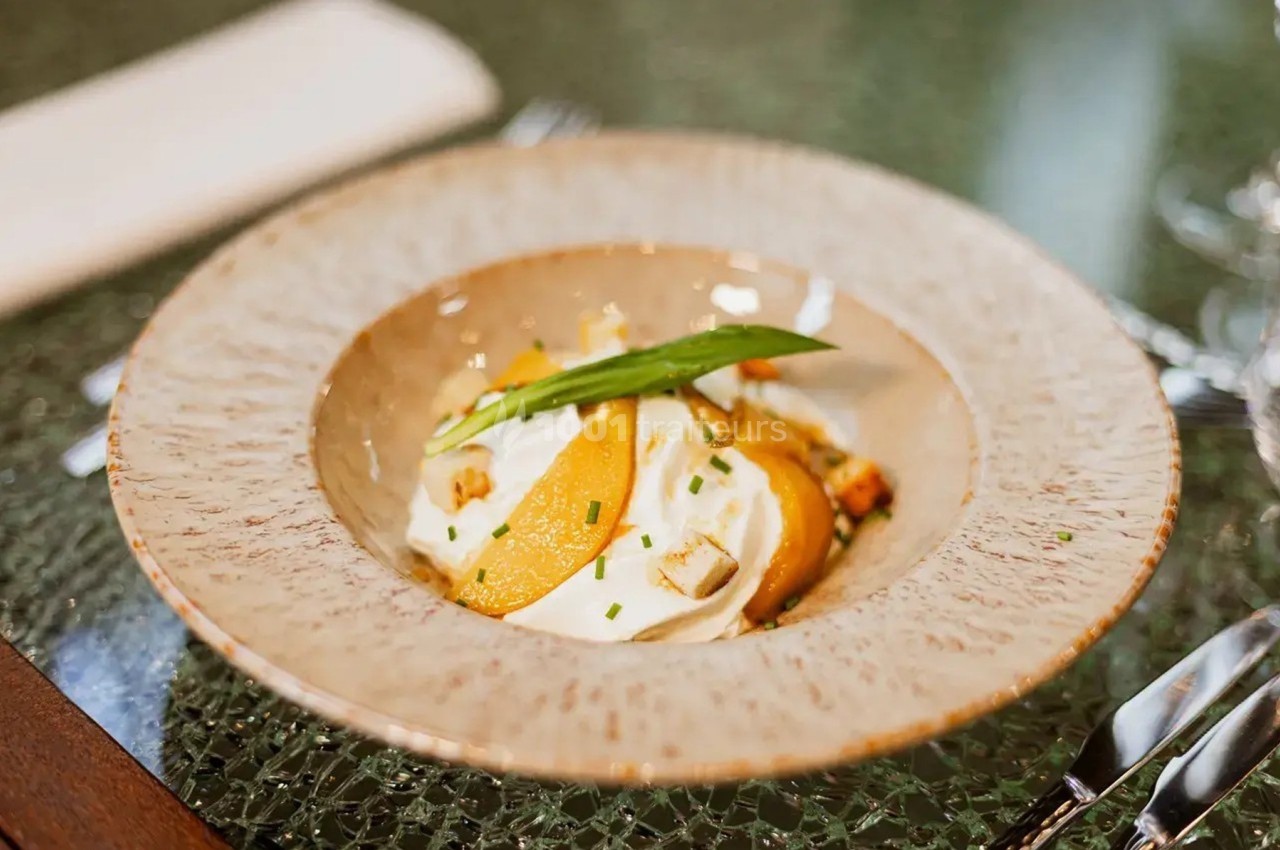 Assiette creuse contenant une préparation gourmande avec des tranches de poire, crème et herbes fraîches, sur une table.