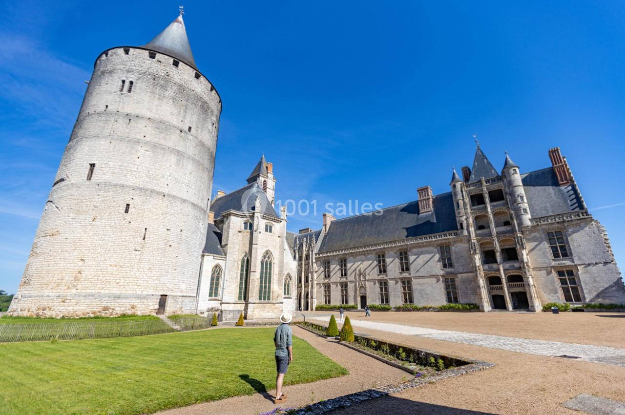 Vue d'un château historique avec une tour ronde, une aile gothique et une cour, sous un ciel bleu dégagé.
