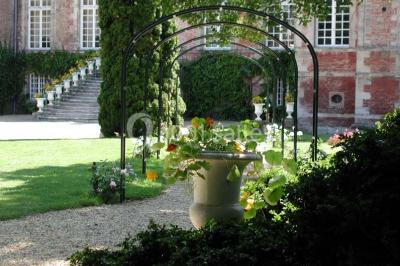 Façade d'un château en briques rouges et blanches avec un toit en ardoise, entouré d'un jardin bien entretenu.