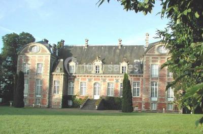 Façade d'un château en briques rouges et blanches avec un toit en ardoise, entouré d'un jardin bien entretenu.