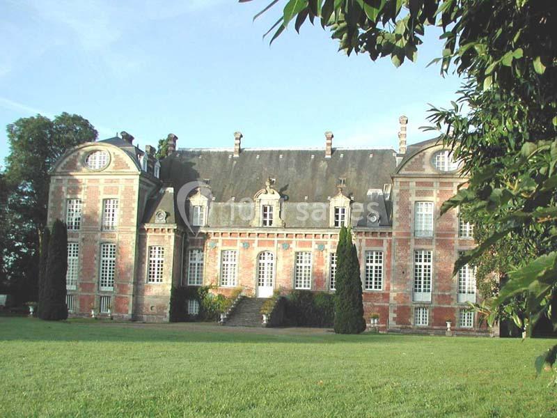 Façade d'un château en briques rouges et pierres blanches, entouré de pelouse et d'arbres.