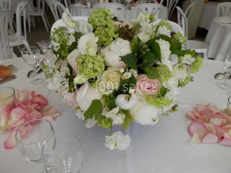 Centre de table floral avec roses, pivoines et feuillage, entouré de pétales roses sur une nappe blanche.