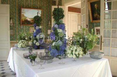 Façade d'un château en briques rouges et blanches avec un toit en ardoise, entouré d'un jardin bien entretenu.