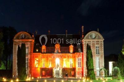 Façade d'un château en briques rouges et blanches avec un toit en ardoise, entouré d'un jardin bien entretenu.