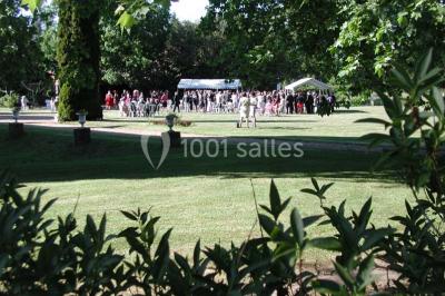 Façade d'un château en briques rouges et blanches avec un toit en ardoise, entouré d'un jardin bien entretenu.