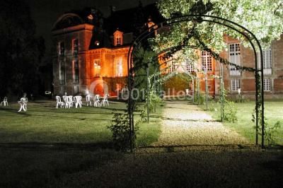 Façade d'un château en briques rouges et blanches avec un toit en ardoise, entouré d'un jardin bien entretenu.