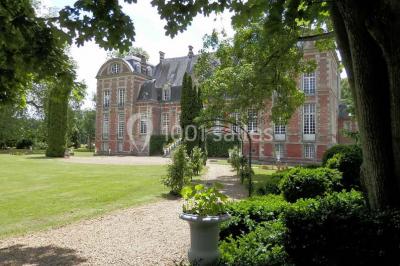 Façade d'un château en briques rouges et blanches avec un toit en ardoise, entouré d'un jardin bien entretenu.
