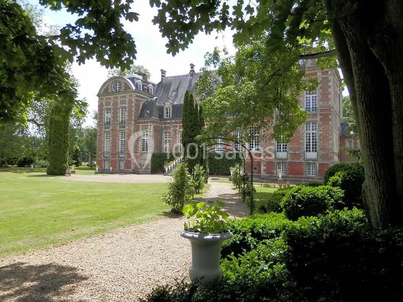 Façade d'un château en briques rouges entouré d'un parc arboré avec pelouse et allée gravillonnée.