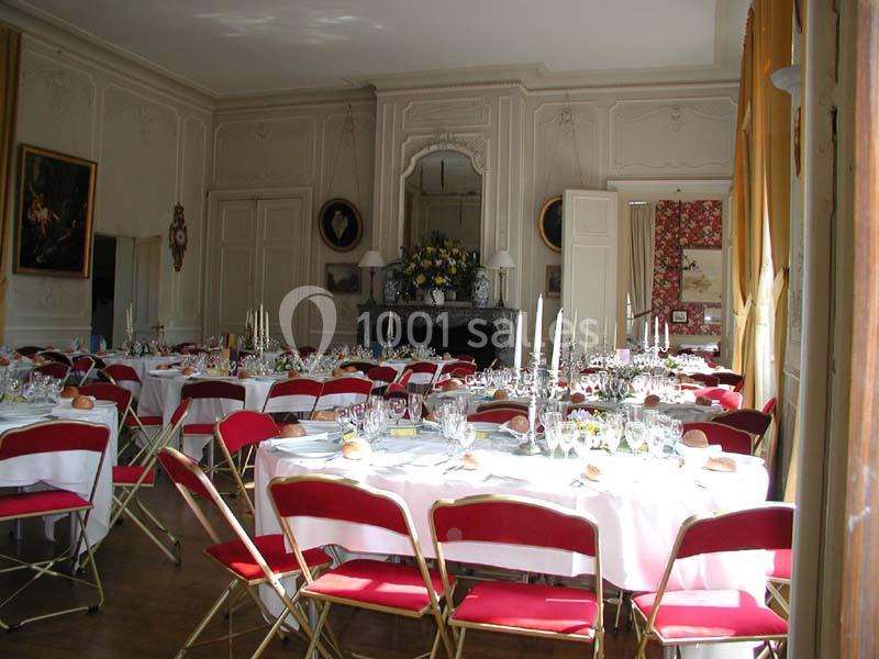 Salle de réception élégante avec tables dressées, nappes blanches, chaises rouges et décorations florales.
