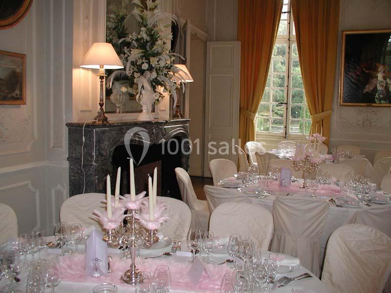 Salle élégante décorée pour un événement, avec tables dressées, nappes blanches, bougies et arrangements floraux.