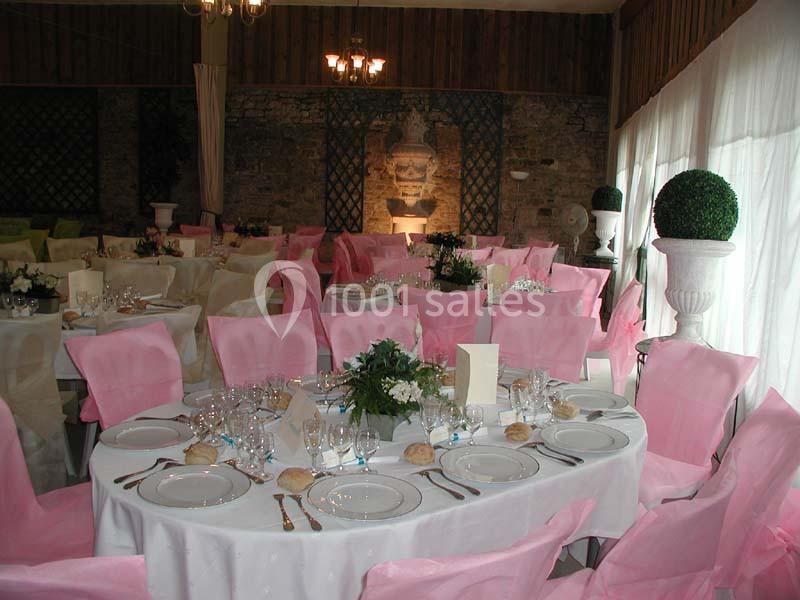 Salle de réception décorée avec des tables rondes dressées, nappes blanches et chaises couvertes de housses roses.