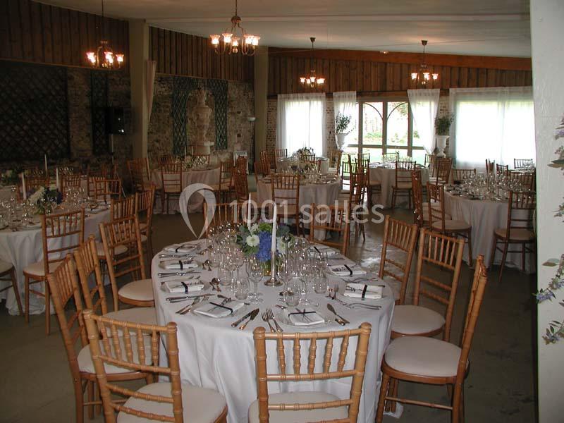 Salle de réception décorée avec des tables rondes dressées, chaises en bois et lumière naturelle entrant par les fenêtres.