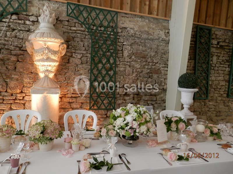 Table de réception décorée de fleurs pastel, disposée devant un mur en pierre avec des éléments décoratifs.