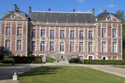 Façade d'un château en briques rouges et blanches avec un toit en ardoise, entouré d'un jardin bien entretenu.