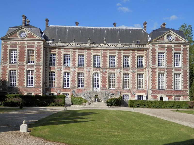 Façade d'un château en briques rouges et blanches avec un toit en ardoise, entouré d'un jardin bien entretenu.