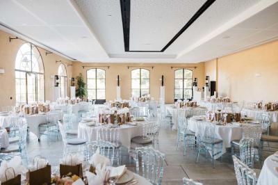 Table dressée avec nappes blanches, verres à vin, couverts, petits pains et centre de table floral dans une salle lumineuse.
