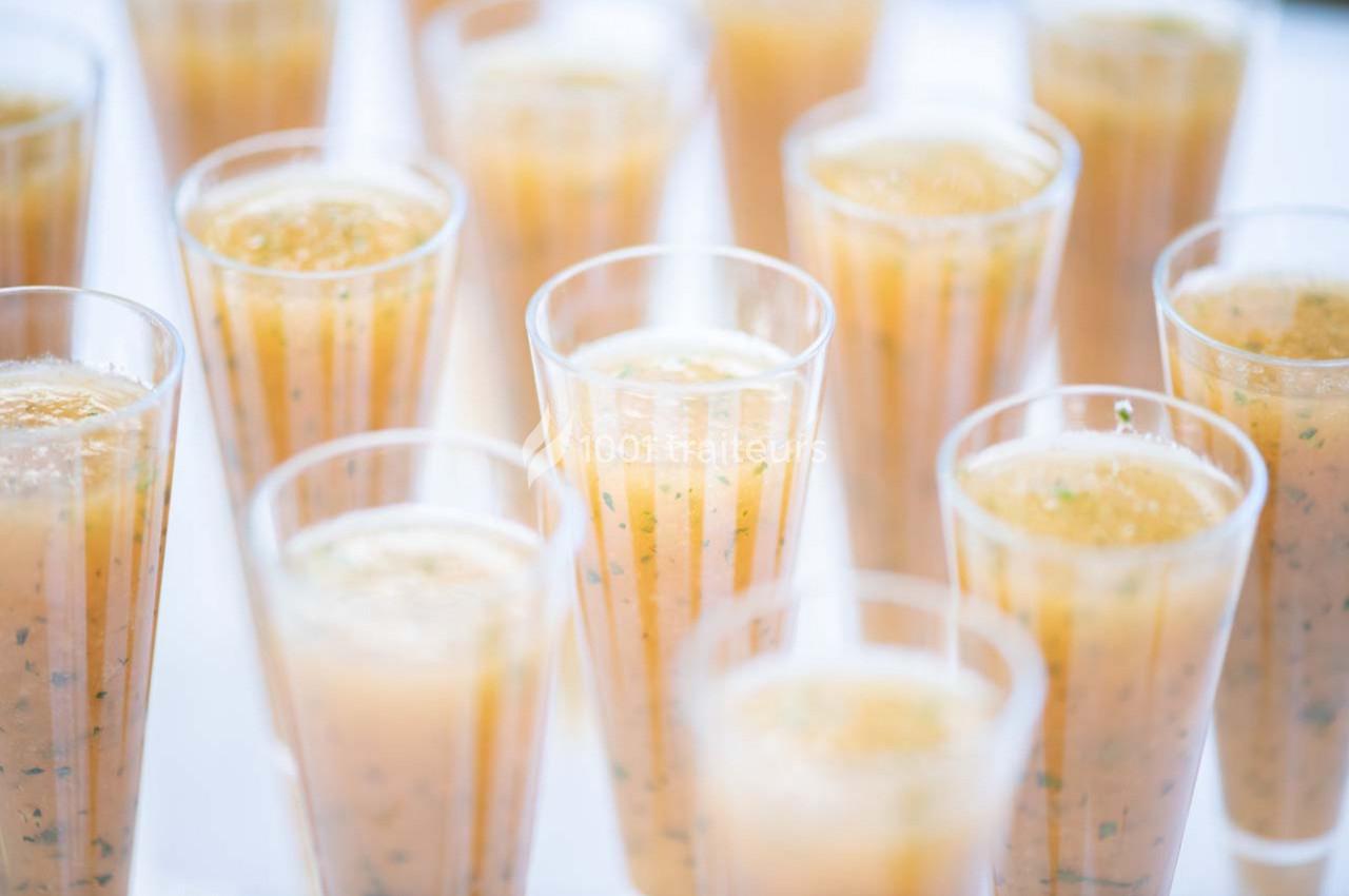 Verres transparents remplis d'une soupe froide orangée, garnie de fines herbes, disposés sur une table blanche.