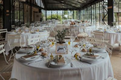 Table dressée avec nappes blanches, verres à vin, couverts, petits pains et centre de table floral dans une salle lumineuse.